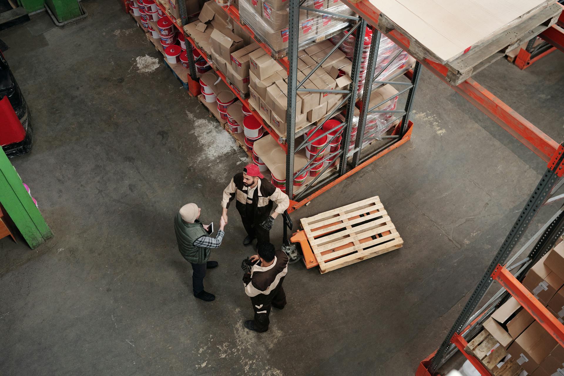 Arbeiter in Logistik-Lager unterhalten sich, Drohnenaufnahme.