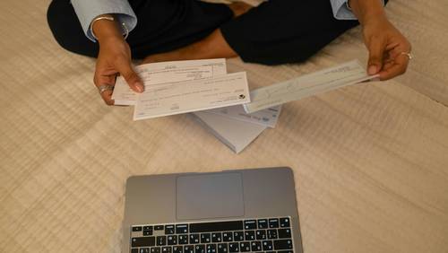 Person vor Laptop mit Schecks in der Hand