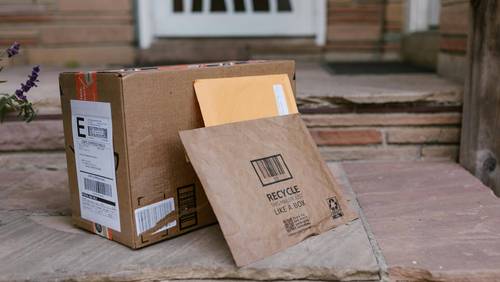 Paket und Versandtasche mit Versandetikett vor Haustür