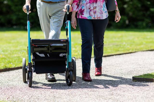Person mit Rollator auf einem Gehweg.