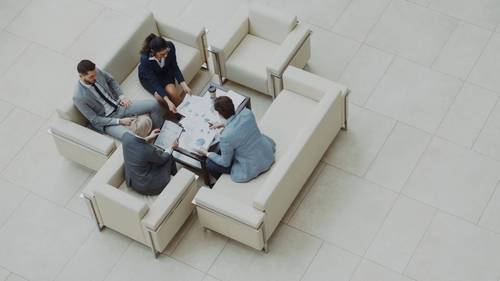 Vier Personen sitzen in einer hellen Bürolobby um einen Tisch mit Unterlagen, aufgenommen von oben.