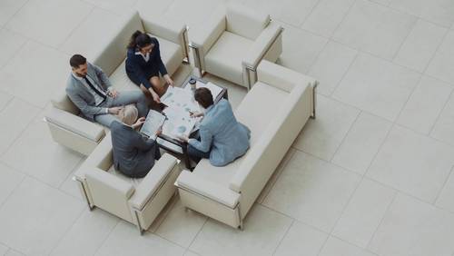 Vier Personen sitzen in einer hellen Bürolobby um einen Tisch mit Unterlagen, aufgenommen von oben.