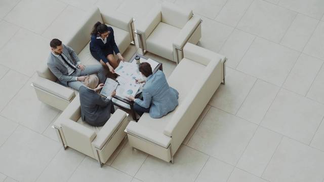 Schufa-Schattendatenbank: Finanzierungsgespräch von oben Vier Personen sitzen in einer hellen Bürolobby um einen Tisch mit Unterlagen, aufgenommen von oben.