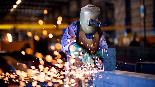 Schweißer arbeitet in einer Industriehalle, während Funken fliegen.