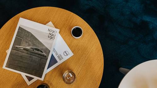 Mehrere Broschüren und Magazine liegen neben einer Kaffeetasse auf einem Holztisch.