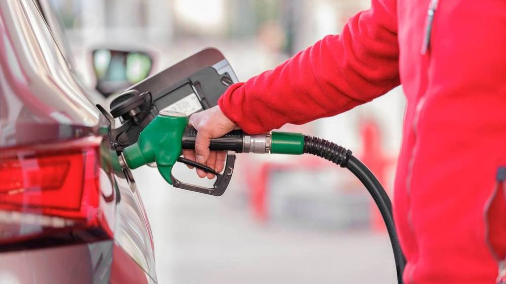 Person betankt ein Auto an einer Tankstelle mit einer grünen Zapfpistole.
