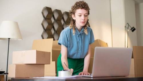 Onlinehändlerin zwischen Versandkartons und Laptop