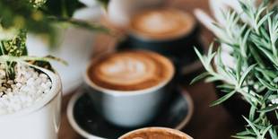 Ein paar Kaffeetassen voller Kaffee und Milch sind auf einem Tisch hintereinander aufgereiht. Foto: Unsplash, Nathan Dumlao