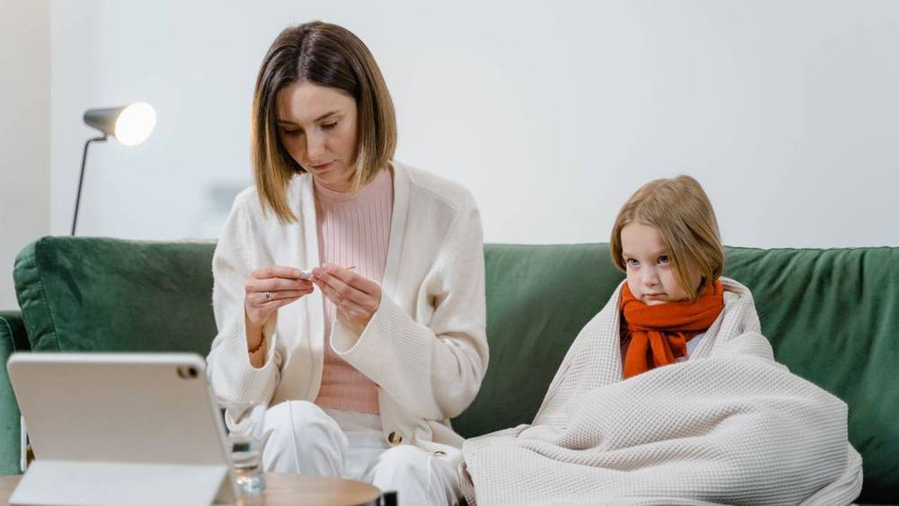 Elternteil arbeitet am Tablet und betreut krankes Kind zu Hause