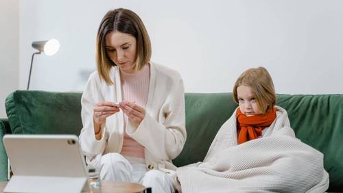 Elternteil arbeitet am Tablet und betreut krankes Kind zu Hause