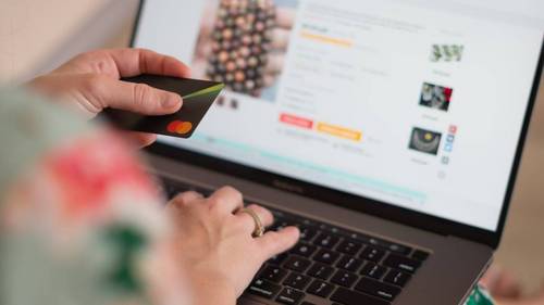 Person hält eine Kreditkarte vor einem Laptop mit geöffnetem Online-Shop