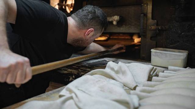 Bäcker schiebt Gebäck in Holzofen