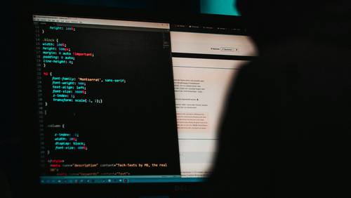 Person sitzt vor Bildschirm. Auf dem Bildschirm: Code-Zeilen.