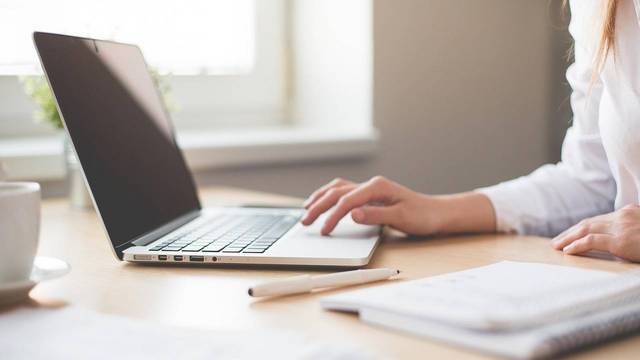 Frau am Laptop Frau tippt auf Laptop. Daneben Notizbuch mit Stift.