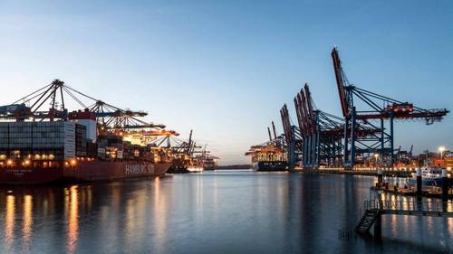 Containerbrücken und ein beladenes Containerschiff im Hamburger Hafen in der Abenddämmerung.