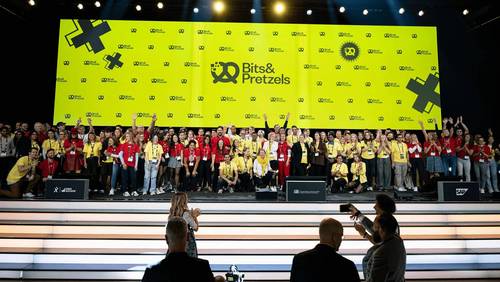 Gruppenfoto des Bits-&-Pretzels-Teams auf der Bühne vor einer gelben LED-Wand mit dem Bits-&-Pretzels-Logo.