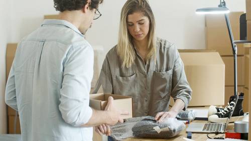 Zwei Personen verpacken Waren für den Versand in Kartons und Luftpolsterfolie.